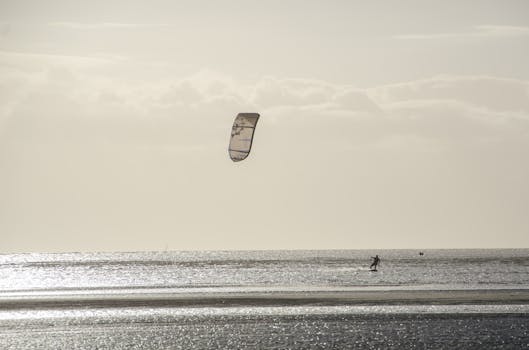 Silhouetted kite surfer enjoying sports on ocean waves during a serene sunset.